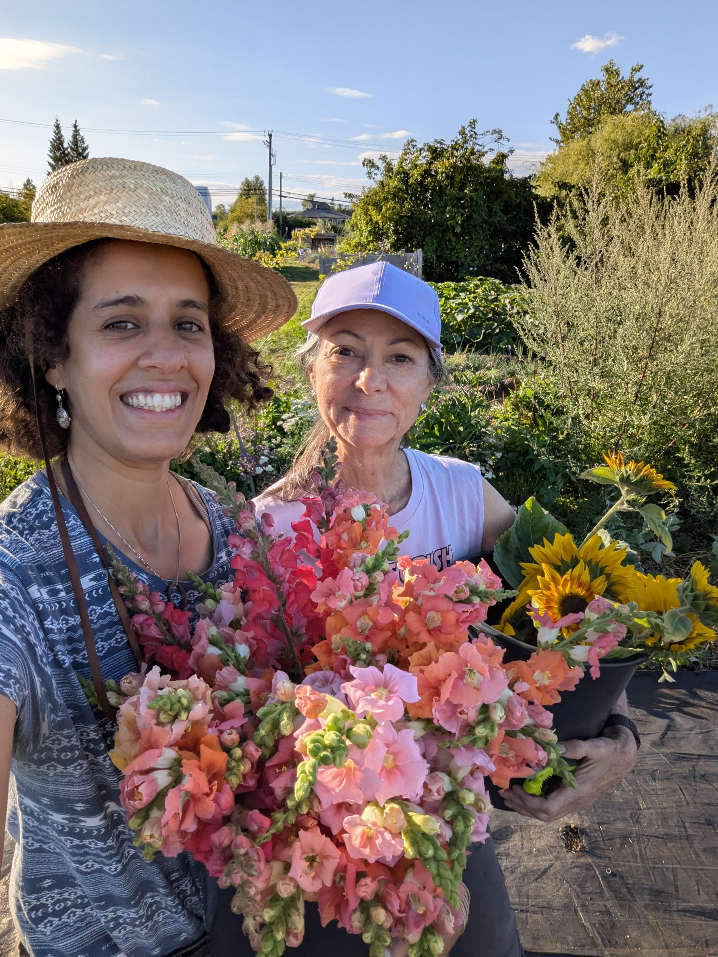 Imene and her mom in the garden holding armfuls of coral snapdragons and sunflowers