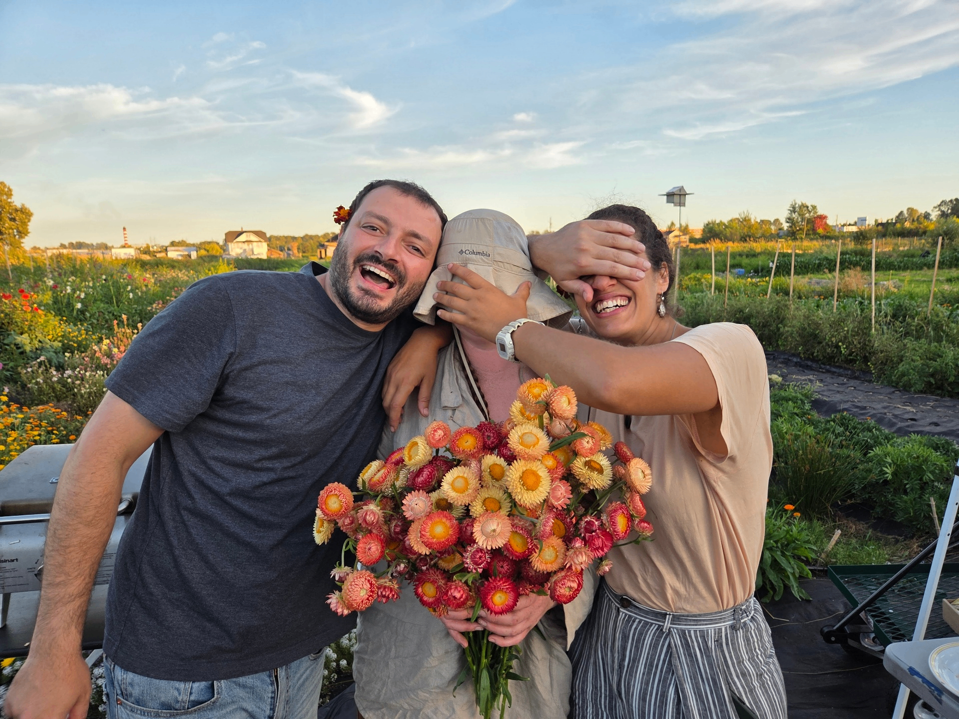 Imene with two friends in the garden, holding a bouquet of strawflowers at sunset