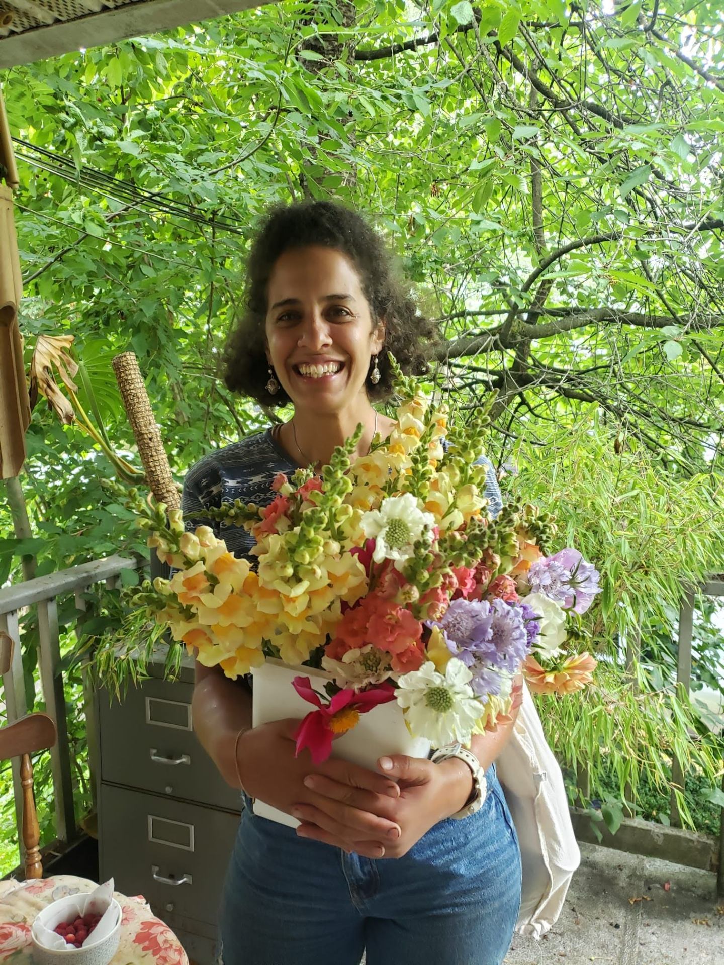 Imene smiling with a hand-tied bouquet of snapdragons and scabiosa