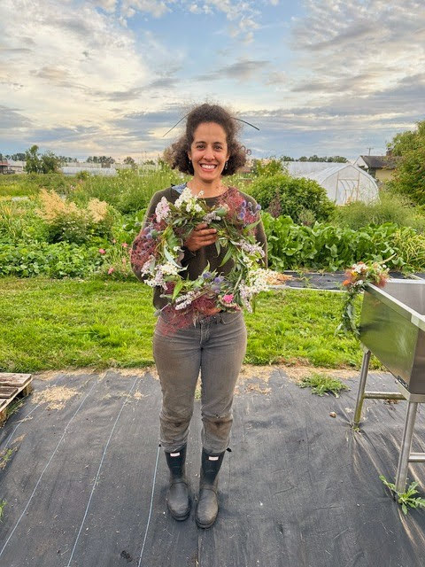 Imene holding a hand-woven flower wreath in the garden at golden hour